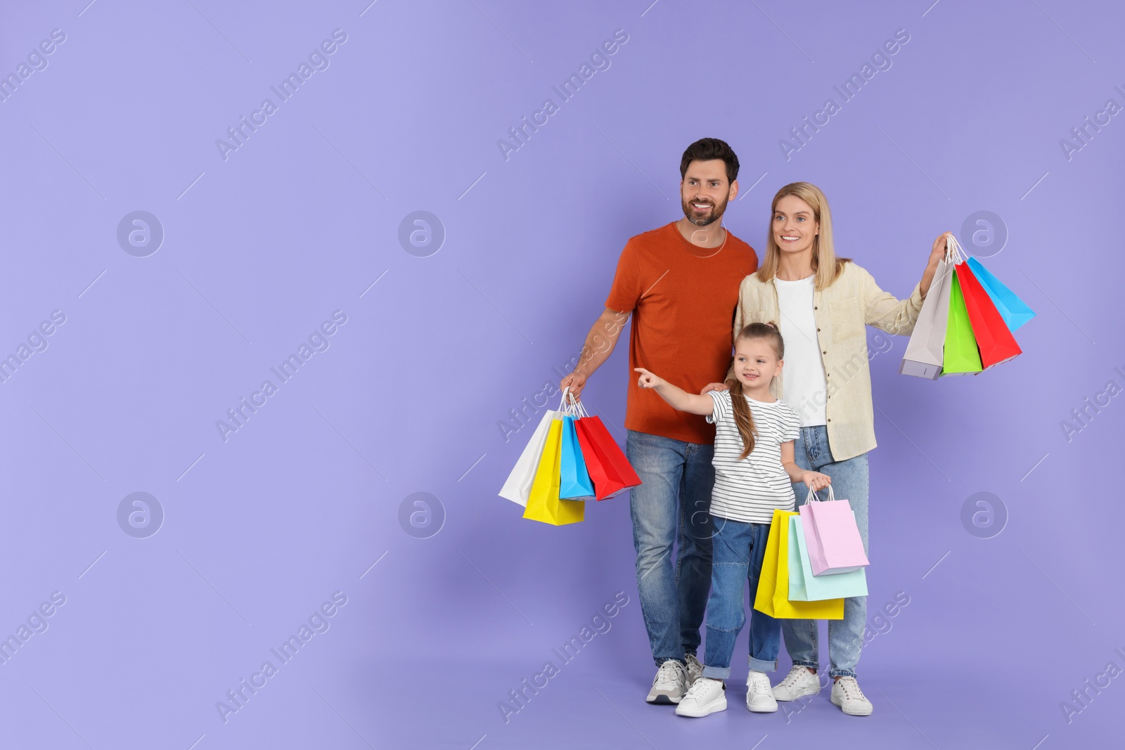 Photo of Family shopping. Happy parents and daughter with many colorful bags on violet background. Space for text