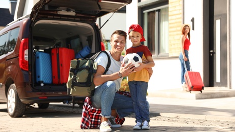 Photo of Happy family near car with suitcases outdoors. Moving day