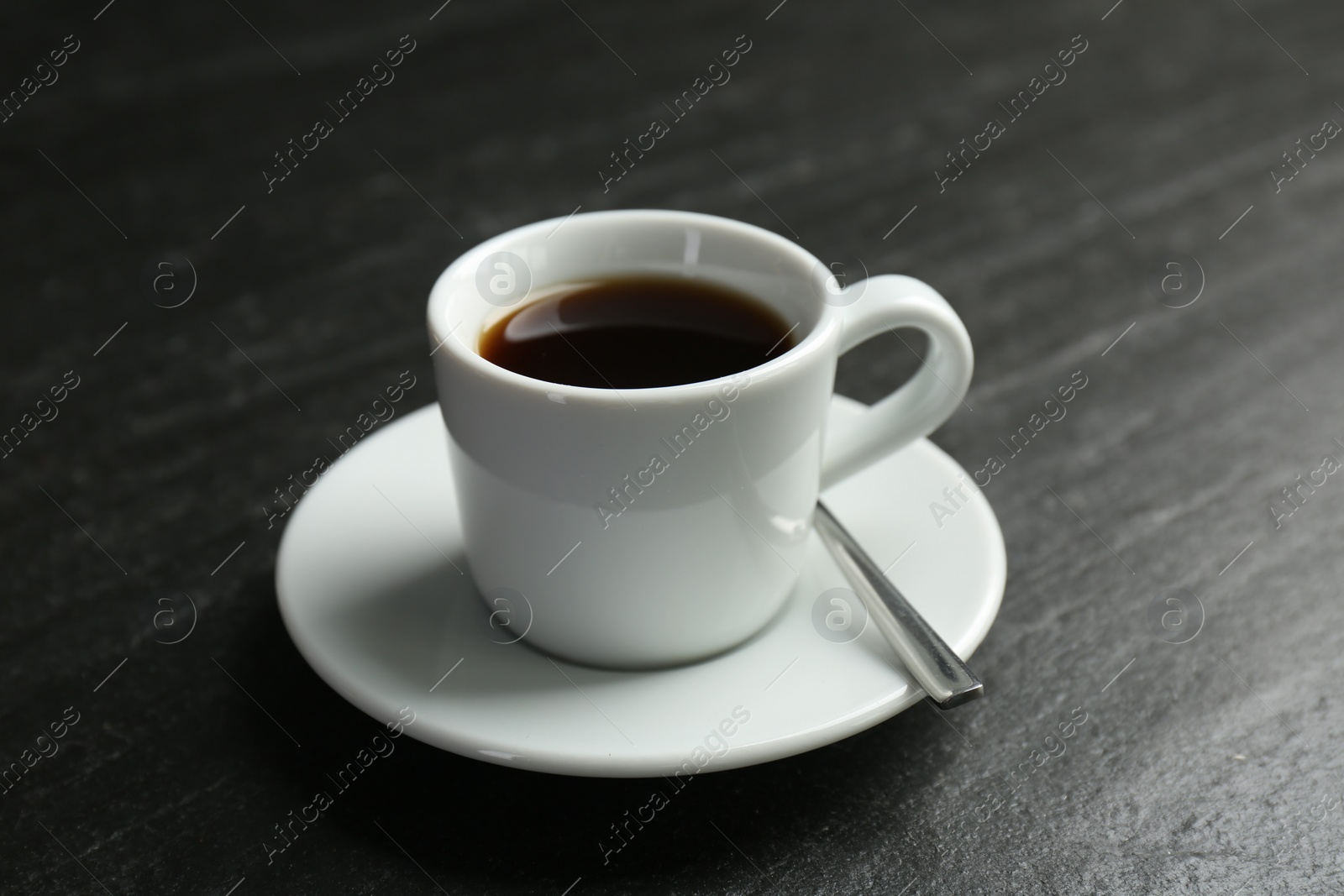 Photo of Hot coffee in cup and saucer on dark textured table, closeup