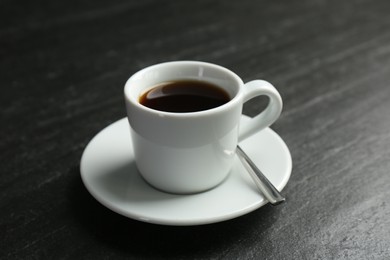 Photo of Hot coffee in cup and saucer on dark textured table, closeup