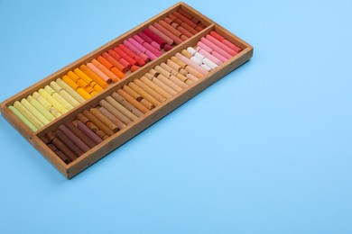 Photo of Set of soft pastels in wooden box on light blue background. Drawing material