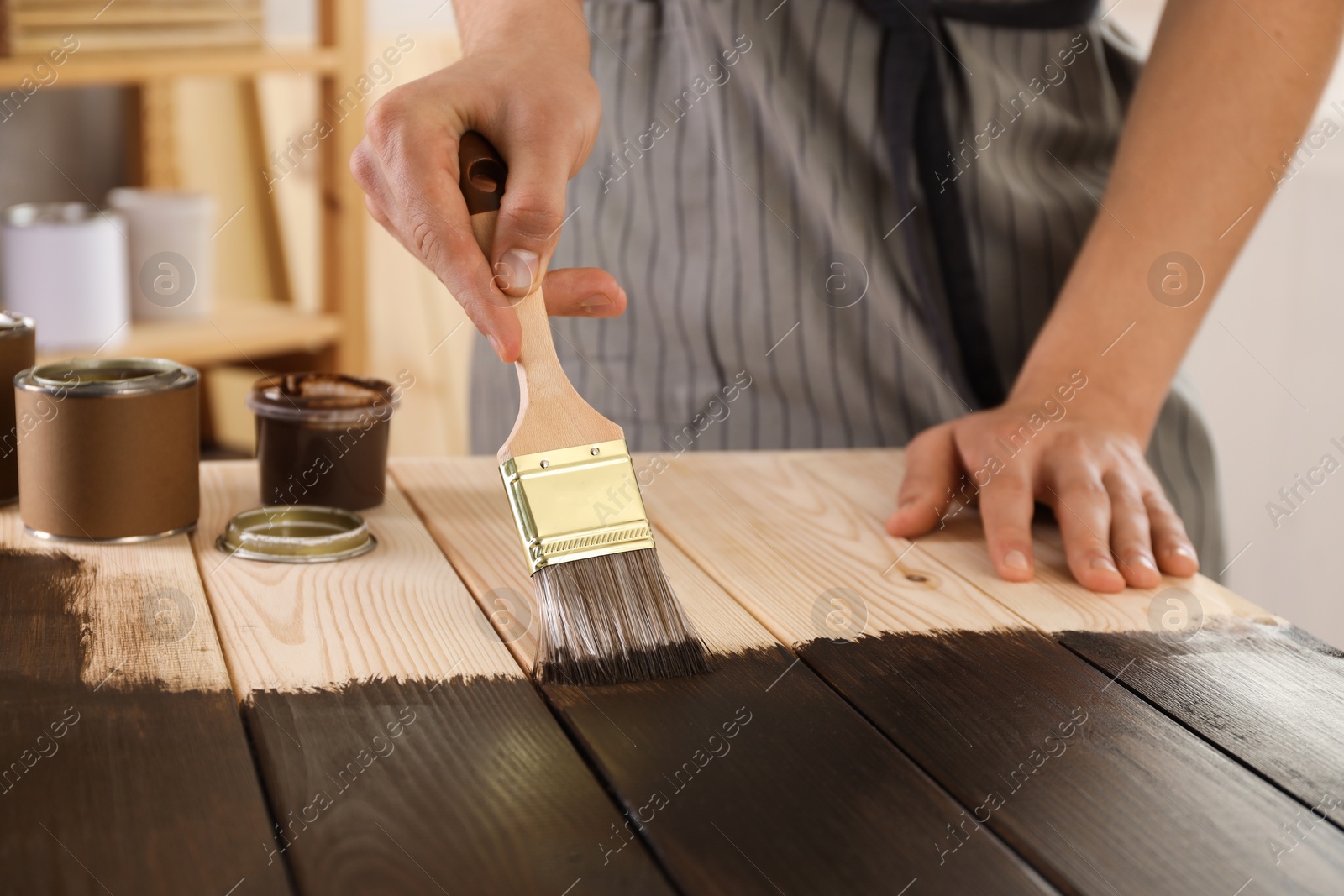 Photo of Man with brush applying wood stain onto wooden surface indoors, closeup