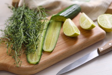 Photo of Fresh tarragon leaves, cucumber, lime and knife on white wooden table, closeup