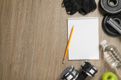 Photo of Notebook, pencil and sports equipment on wooden table, flat lay with space for text. Personal training