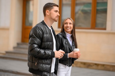 Photo of Lovely young couple with cups of coffee walking together on city street. Romantic date