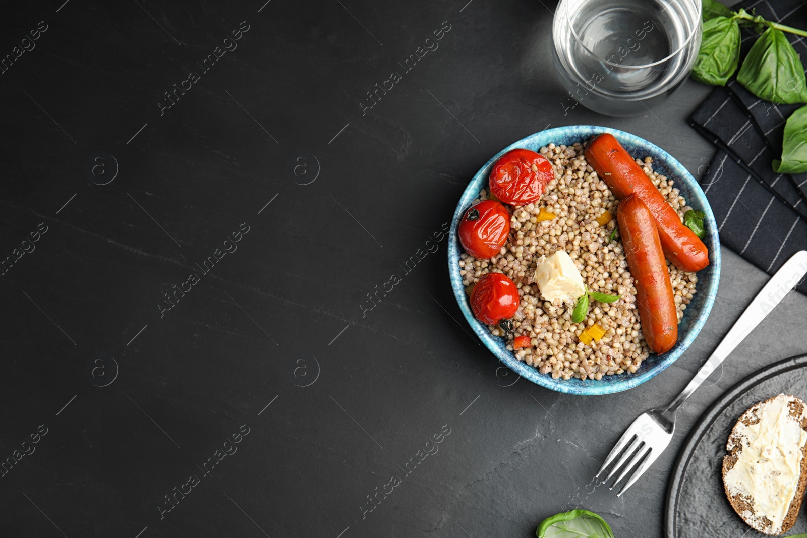 Photo of Tasty buckwheat porridge with sausages on dark grey table, flat lay. Space for text