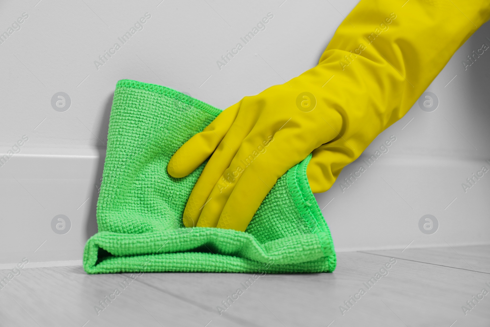 Photo of Woman in gloves cleaning plinth with cloth indoors, closeup