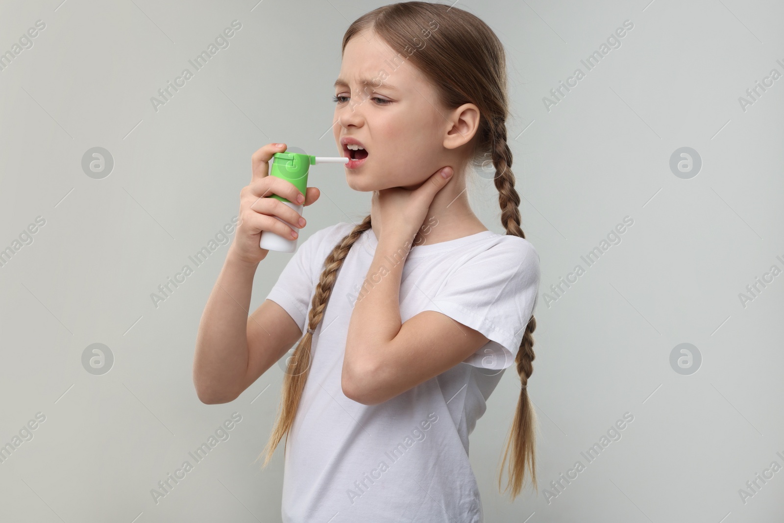 Photo of Little girl using throat spray on light grey background