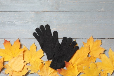 Photo of Stylish black woolen gloves and dry leaves on grey wooden table, flat lay. Space for text