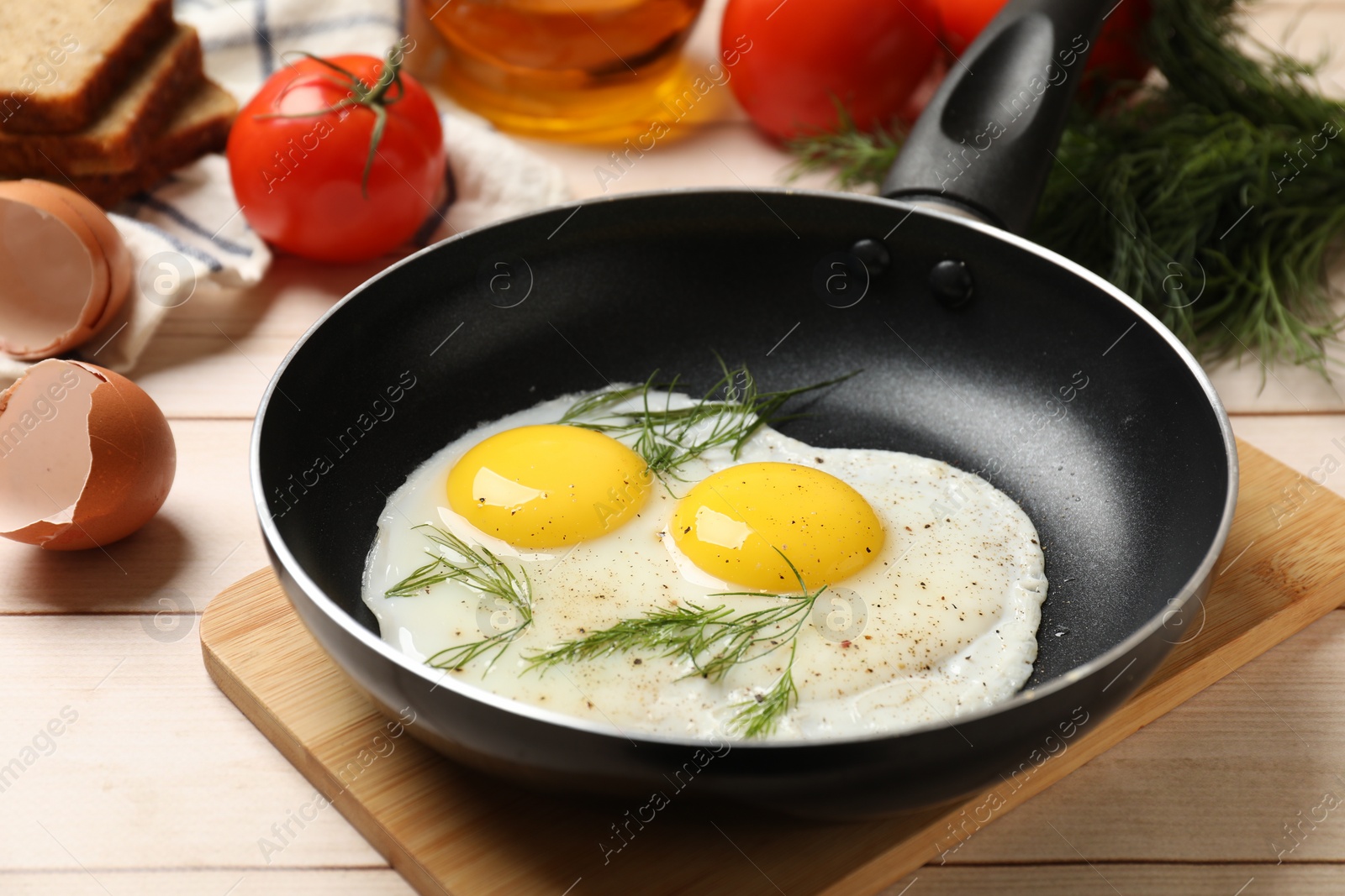 Photo of Frying pan with tasty cooked eggs, dill and other products on light wooden table