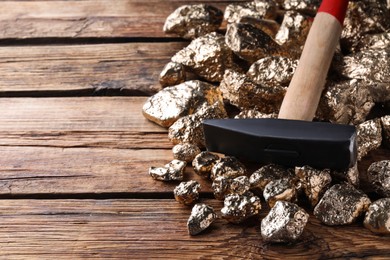 Pile of gold nuggets and hammer on wooden table, closeup. Space for text