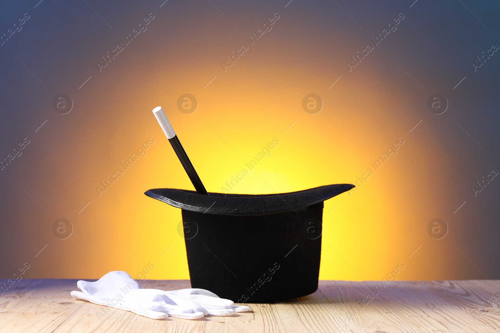 Photo of Magician's hat, wand and gloves on wooden table against color background