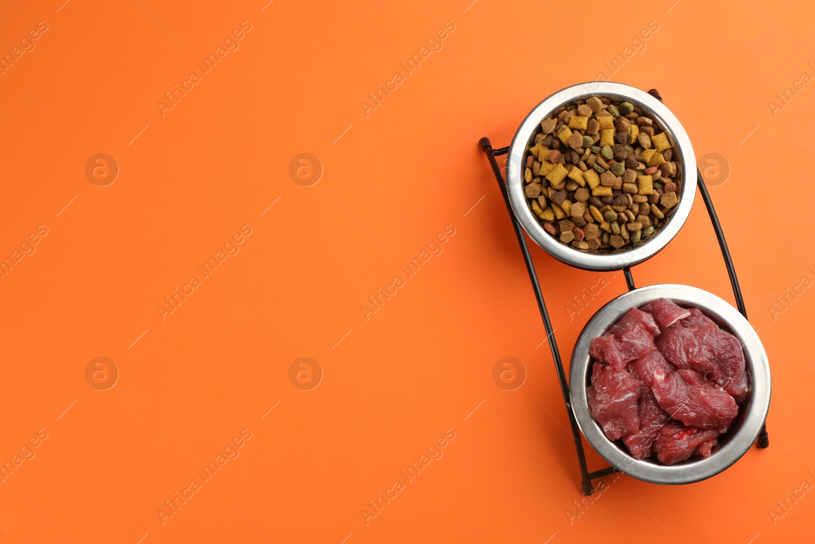 Photo of Pet food and raw meat on orange background, top view. Space for text