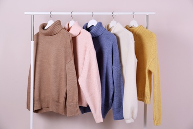 Warm sweaters hanging on rack against pink background