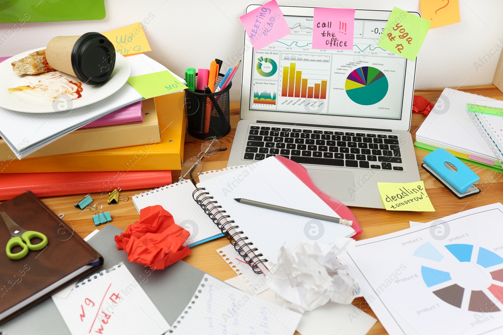 Photo of Messy table with laptop and stationery. Concept of being overwhelmed by work