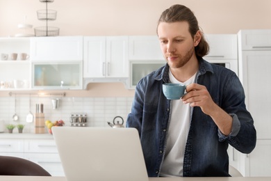 Photo of Young man working with laptop at desk in home office