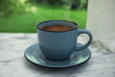 Photo of Cup of hot aromatic coffee on white marble windowsill. Rainy weather