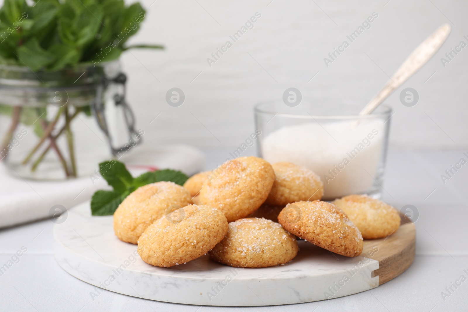 Photo of Tasty sweet sugar cookies, milk and mint on white tiled table, closeup