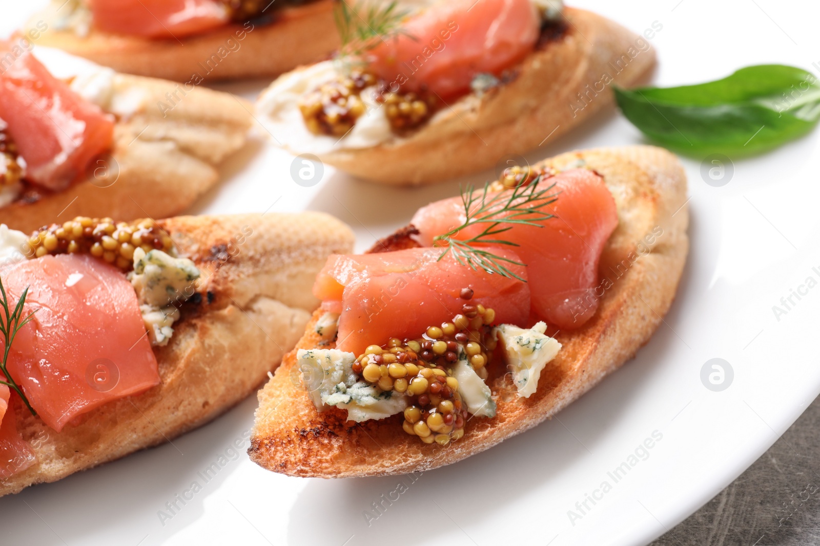 Photo of Tasty bruschettas with salmon and blue cheese on plate, closeup