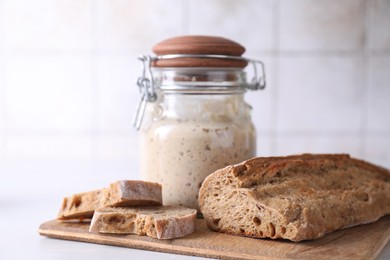 Photo of Sourdough starter in glass jar and fresh bread on light table