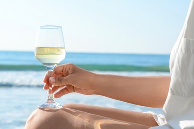 Photo of Woman with glass of tasty wine near sea, closeup