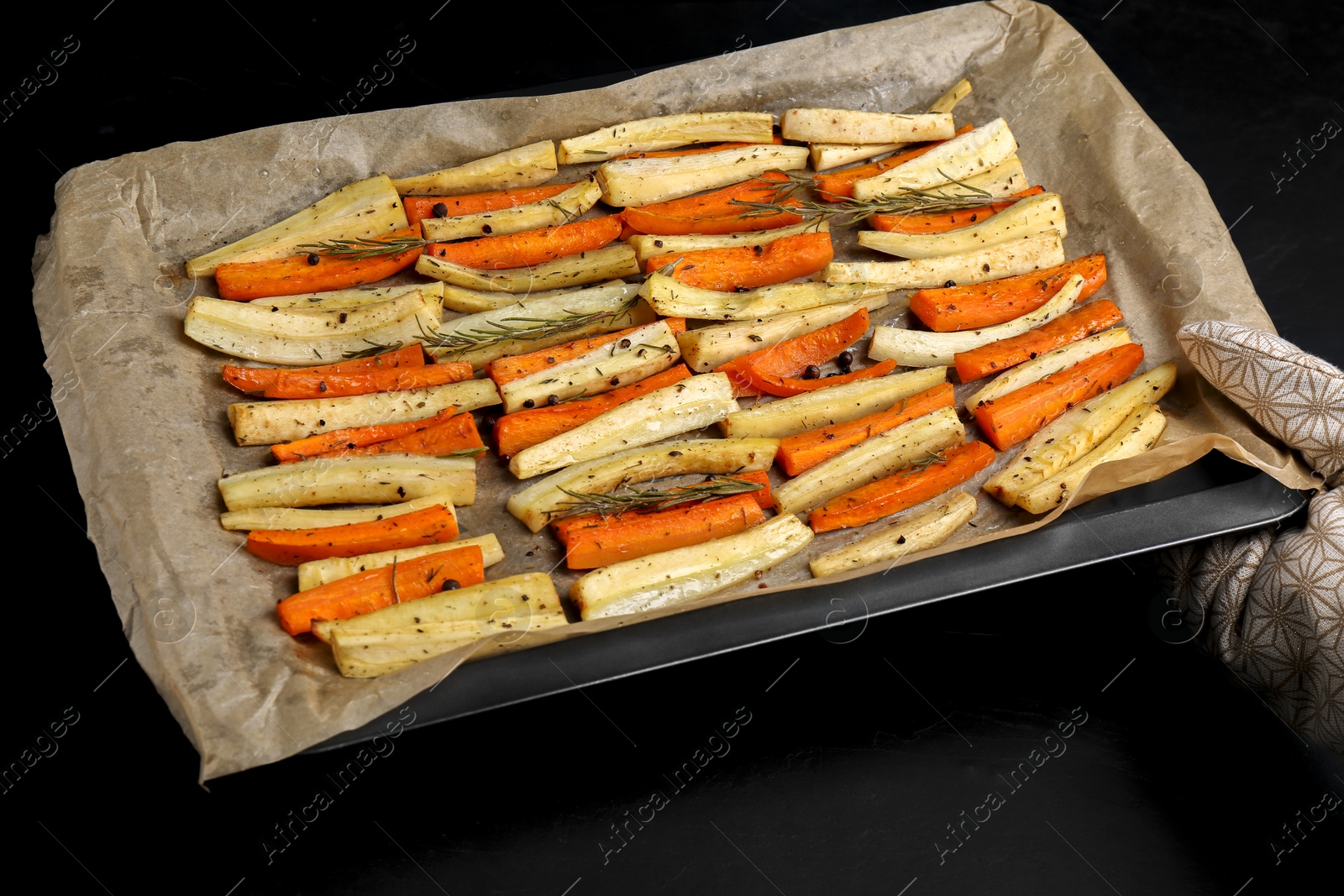 Photo of Tray with parchment, baked parsnips and carrots on black table