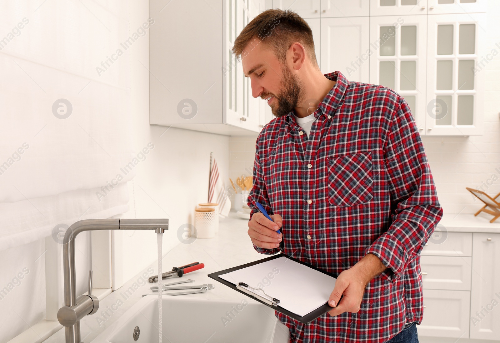 Photo of Plumber with clipboard checking water flow from tap in kitchen. Repair service