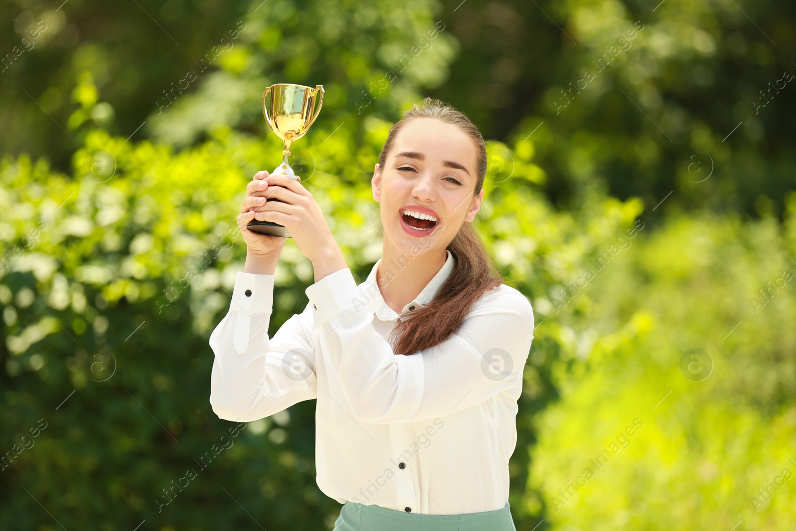 Photo of Portrait of happy young businesswoman with gold trophy cup in green park