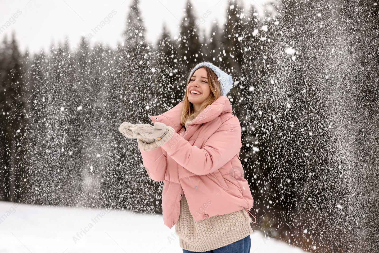 Photo of Young woman in warm clothes catching snow outdoors. Winter vacation