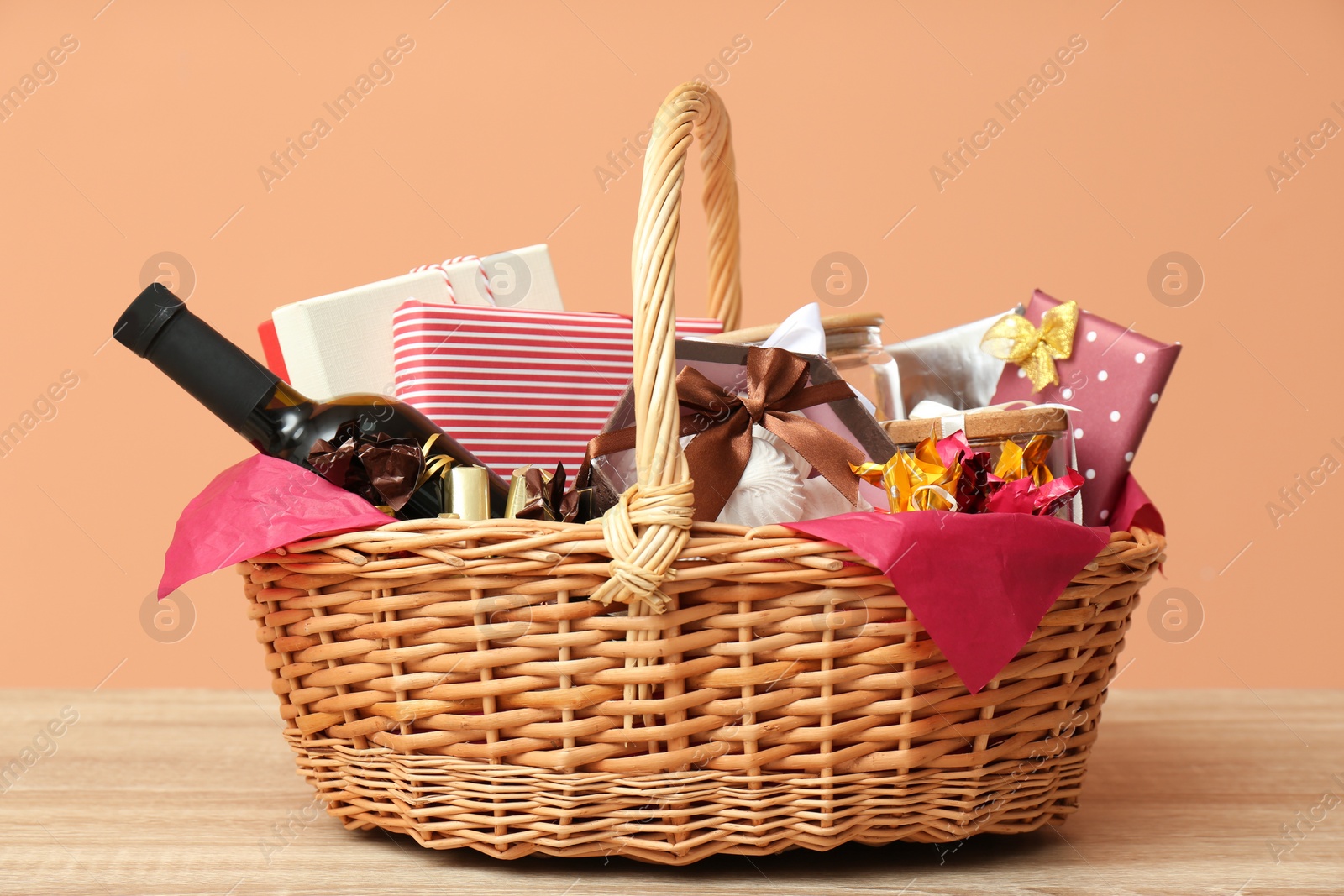 Photo of Wicker gift basket with bottle of wine on wooden table