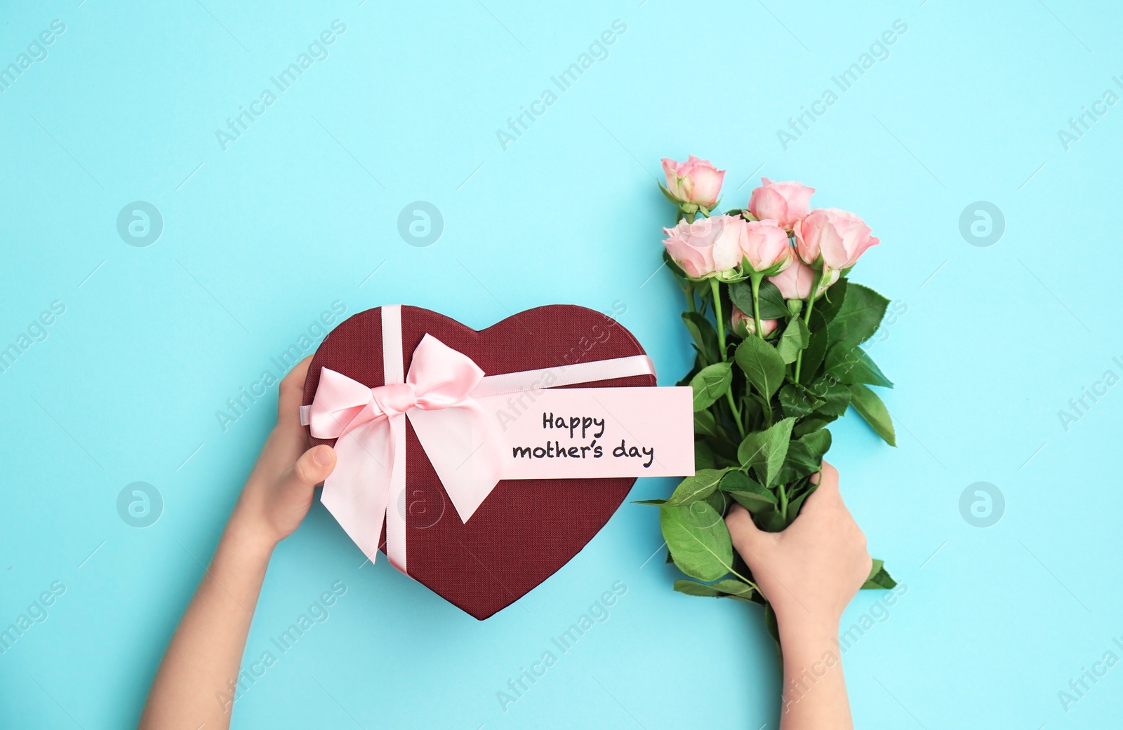 Photo of Child holding gift box and flowers for Mother's Day on color background