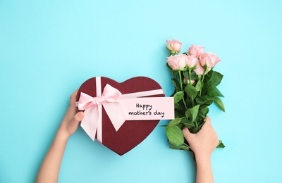 Photo of Child holding gift box and flowers for Mother's Day on color background