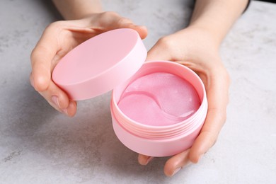 Photo of Woman holding package of under eye patches at light table, closeup. Cosmetic product