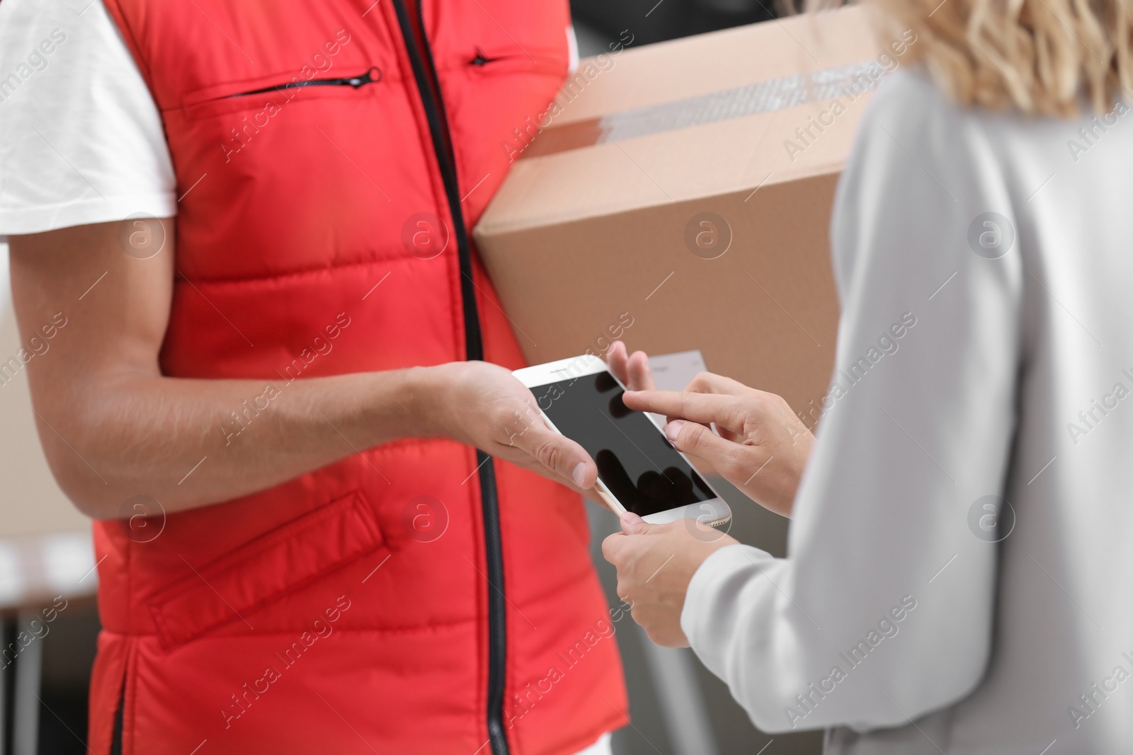 Photo of Woman using smartphone app to confirm receipt of parcel from courier, closeup