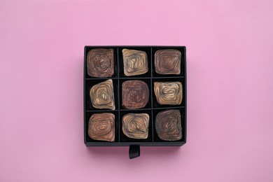 Photo of Box of tasty chocolate candies on pink background, top view