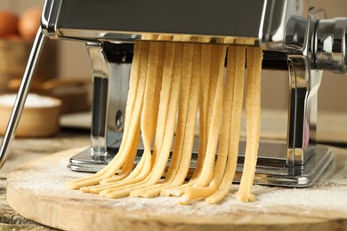 Pasta maker with raw dough on wooden board, closeup