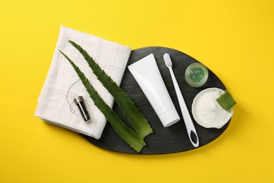 Aloe vera toothpaste in blank tube, brush, green leaves and care products on yellow background, top view. Space for text