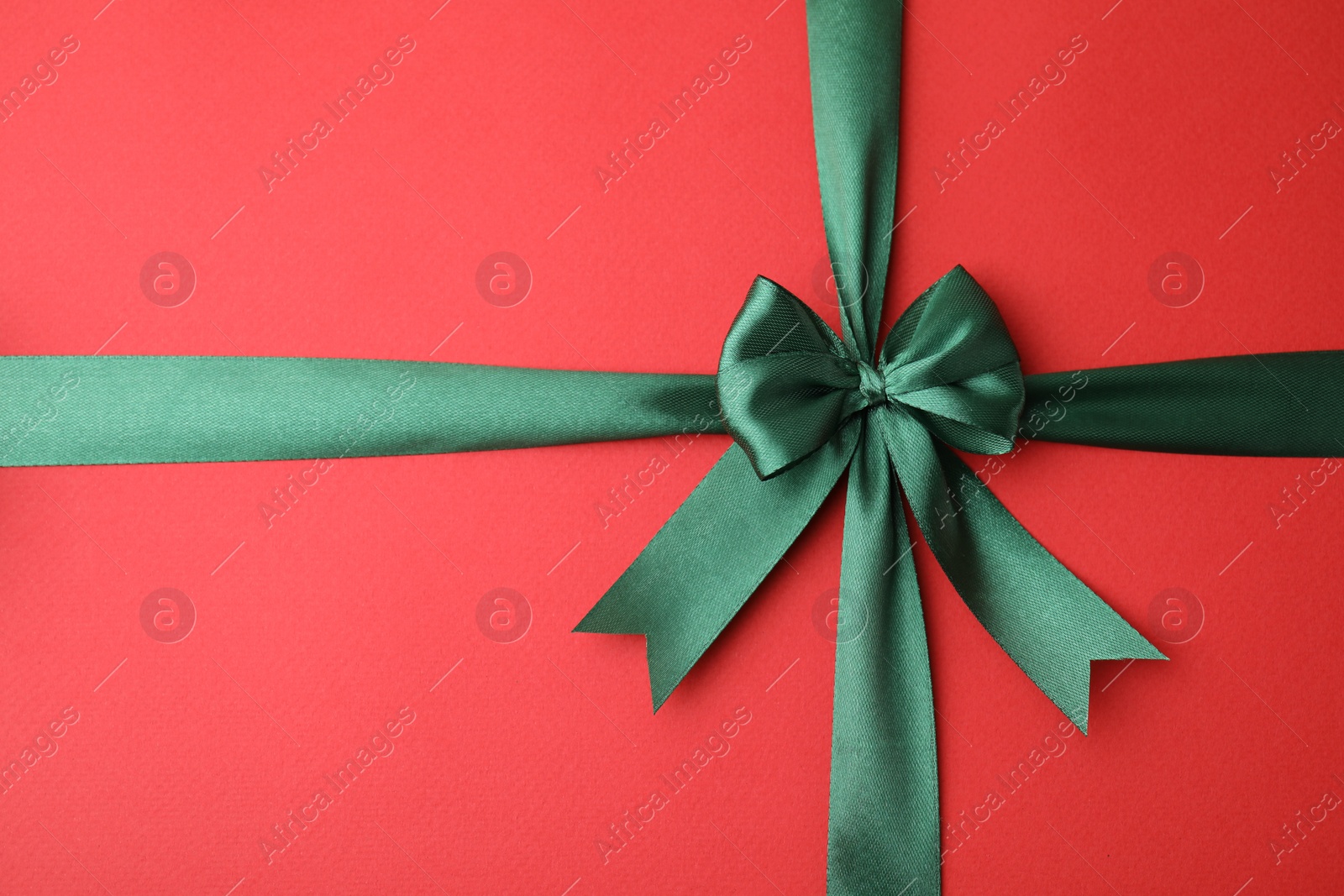 Photo of Green satin ribbon with bow on red background, top view