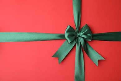 Green satin ribbon with bow on red background, top view