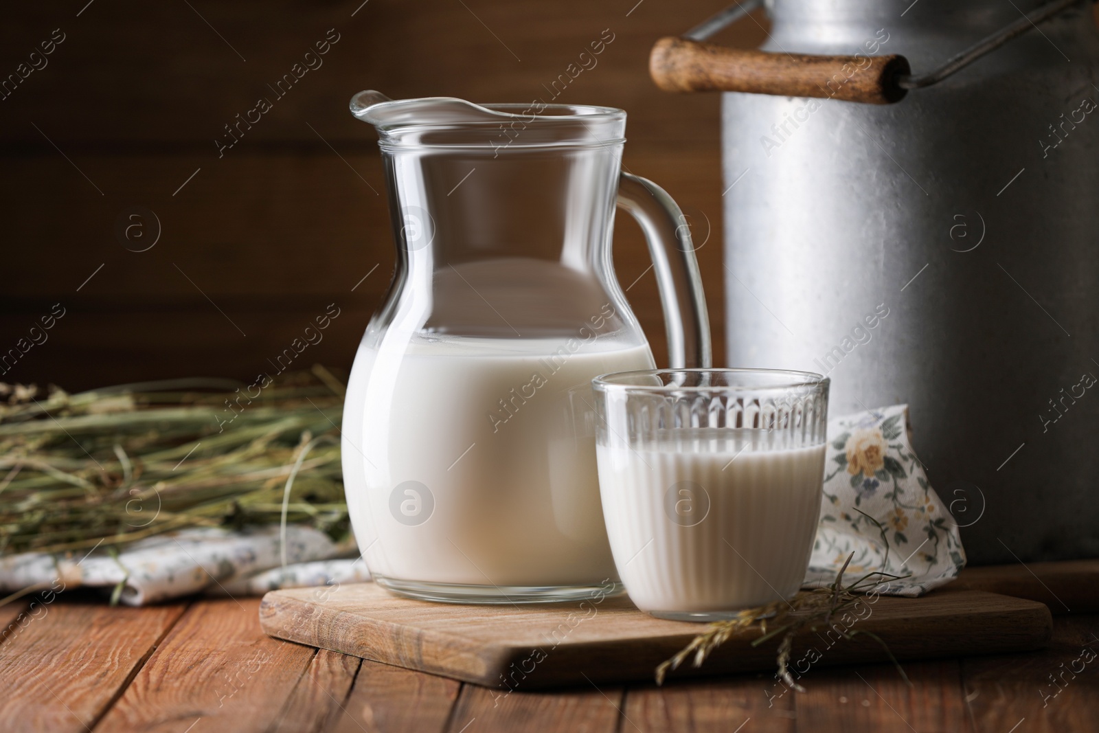 Photo of Tasty fresh milk in can, jug and glass on wooden table. Space for text