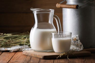 Photo of Tasty fresh milk in can, jug and glass on wooden table. Space for text