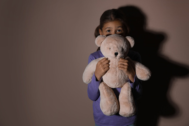 Photo of Sad little girl with teddy bear near beige wall, space for text. Domestic violence concept