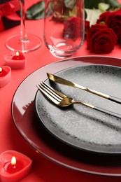 Place setting with heart shaped candles, gift box and bouquet of roses on red table, closeup. Romantic dinner