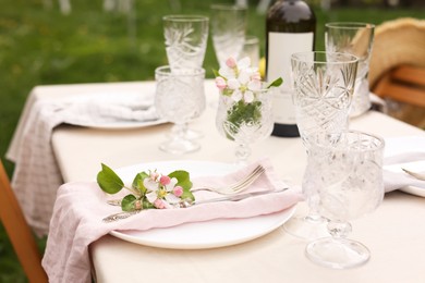 Stylish table setting with beautiful spring flowers, wine, plates and glasses in garden