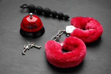 Handcuffs, anal beads and bell with text Ring For Sex on black background