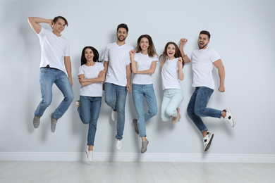 Photo of Group of young people in stylish jeans jumping near light wall