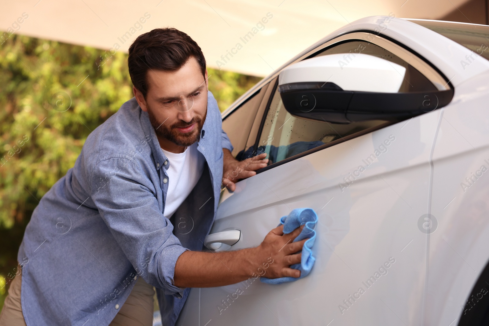 Photo of Bearded man cleaning car door with rag outdoors