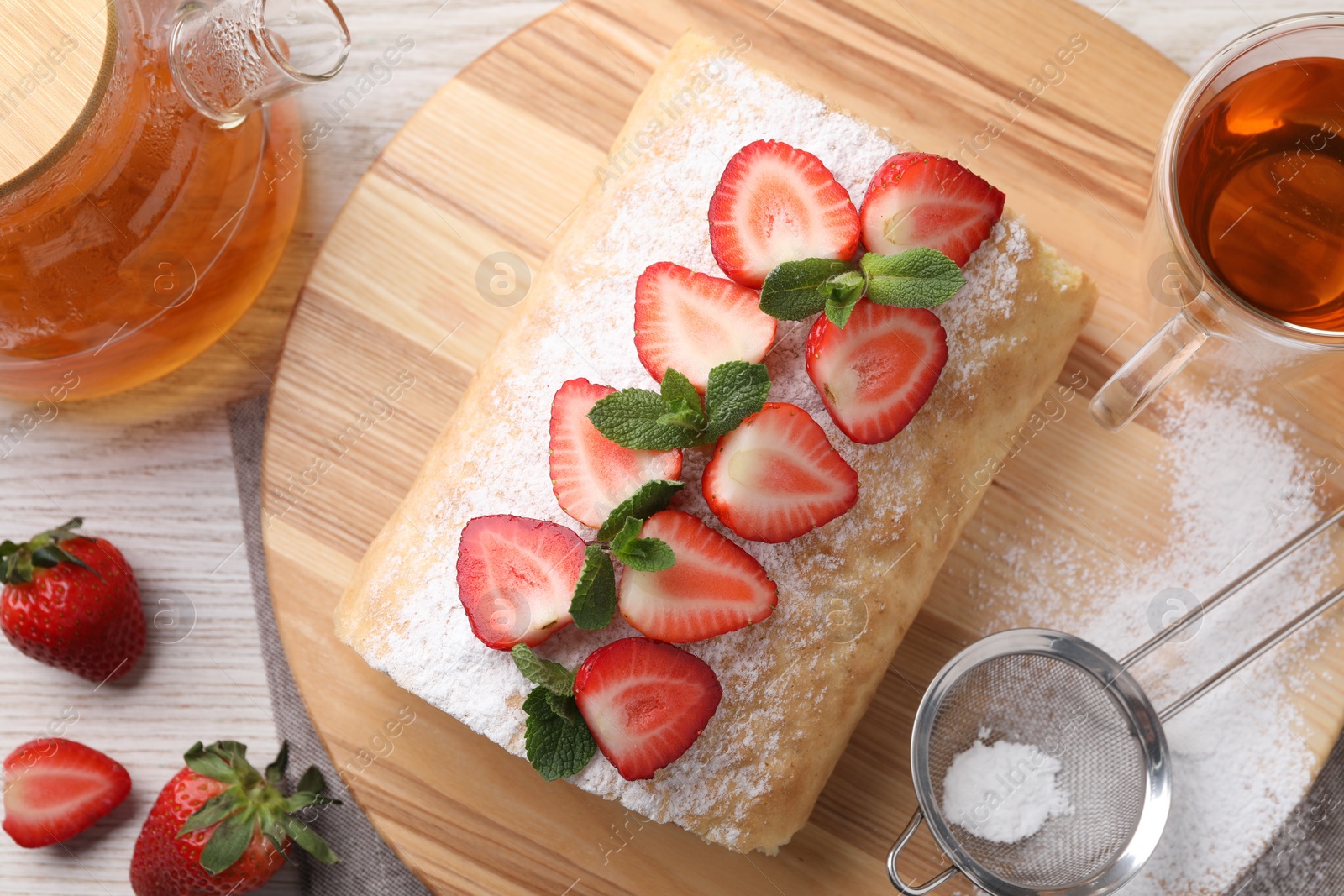 Photo of Delicious cake roll with strawberries and tea on wooden board, flat lay