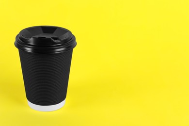Black paper cup with plastic lid on yellow background, space for text. Coffee to go