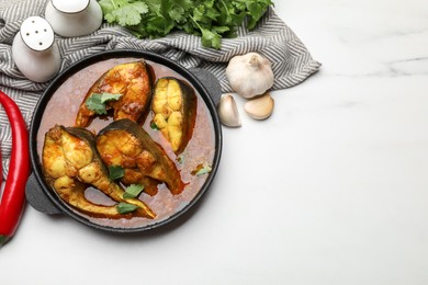 Tasty fish curry and ingredients on white marble table, flat lay. Space for text. Indian cuisine